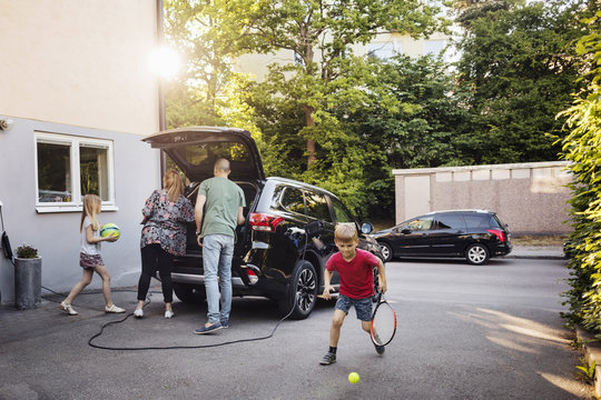 Children playing with balls while parents loading car trunk in back yard