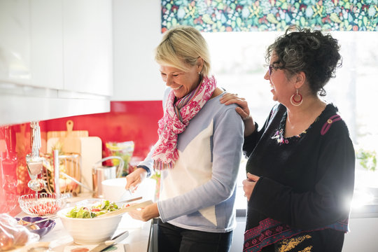 Happy friend talking to woman while preparing salad in brightly lit kitchen
