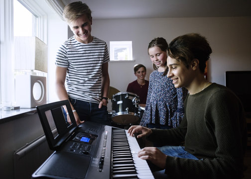 Siblings looking at young man playing piano keyboard in brightly lit room