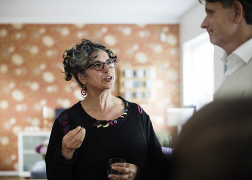 Woman with drink gesturing while talking to man at home