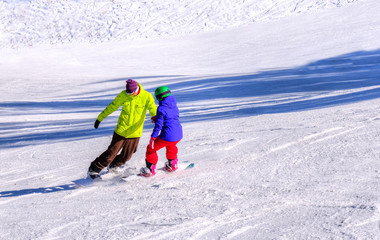 Young couple of people learning snowboard sport outdoor, on the ski slope on mountain. Poiana Brasov resort, Romania