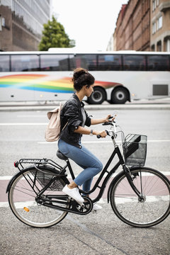 Side view of woman using mobile phone while riding bicycle on city street