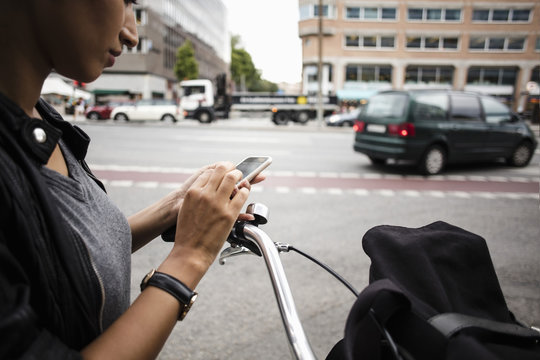 Cropped image of woman with bicycle using mobile phone while standing by street in city