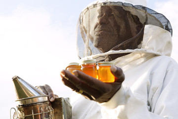 Senior beekeeper holding bee smoker and jars of honey