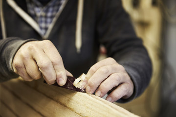 Man standing in a workshop, shaping a wooden surfboard using a hand held plane.