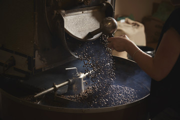 Person opening metal shute and coffee beans falling into roasting drum