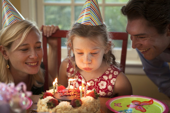 Mother, father and daughter (6-7) blowing out birthday candles