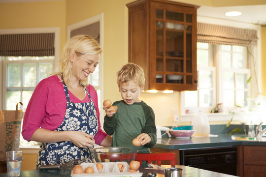 Mother and son (2-3) cracking eggs in bowl