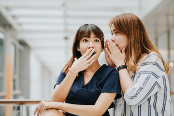 Young Asian girl whispering gossip or secret to her friend with surprise face