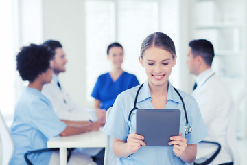 happy doctor with tablet pc over team at clinic