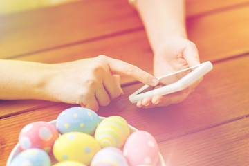 close up of hands with easter eggs and smartphone