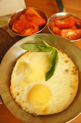 Fried eggs at frying pan with tomato background