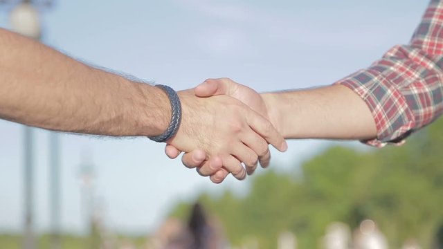 Shaking hands between friends. Friendship handshake outdoor. Two good guys are shaking hands and fists when meeting.
