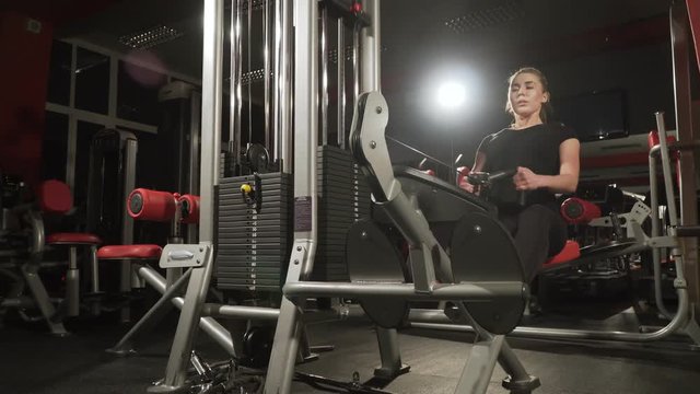Girl in the gym. Weight training. Work on the muscles of the back. Women working out on rowing machine in gym. Women on the exercise machine with a weighting compound. The woman lifts heavy weight in