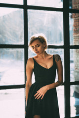 beautiful blonde in a little black dress near a large window