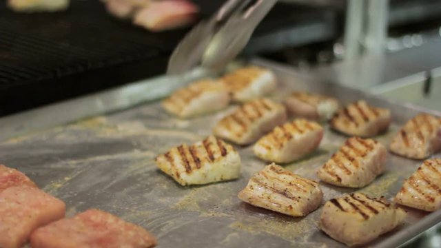 Chef moving salmon fillet from the grill to a tray.