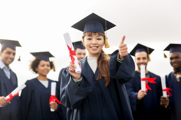happy students with diplomas showing thumbs up