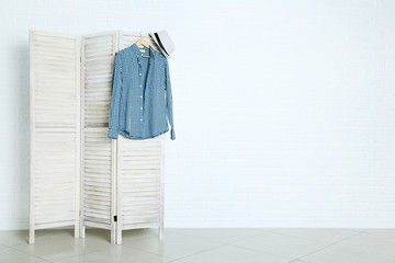 Male shirt and hat hanging on folding screen on brick wall background