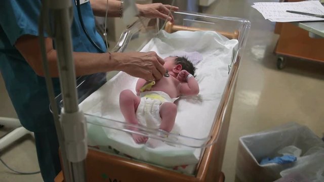 A newborn baby getting check in a bassinet by a nurse.