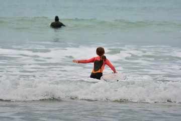 Une jeune surfeuse entre dans l'eau sur une plage en Bretagne