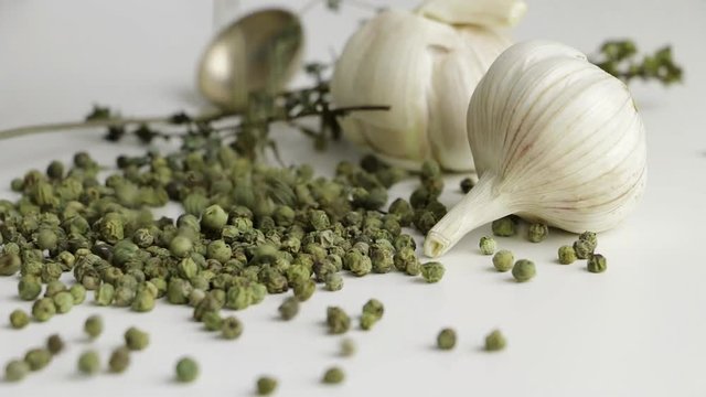 Green peppercorns - pepe verde - famous spice of italian cuisine on white table with garlic bulbs, thyme twig and spoon. Pouring green pepercorns on white table.