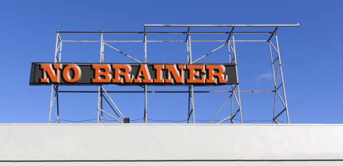 NO BRAINER concept sign attached to empty billboard frame against blue sky.