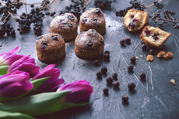 Obraz na płótnie Canvas muffin with currants on a dark background next to the berries on the branches. and a bouquet of flowers. in a rustic style. dark style