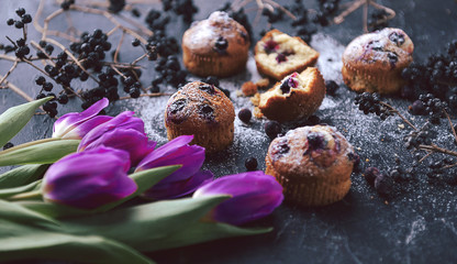 muffin with currants on a dark background next to the berries on the branches. and a bouquet of flowers. in a rustic style. dark style