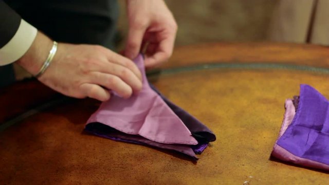 Man in a suit folding a purple handkerchief for his pocket.