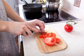 woman cuts tomatoes with a knife on the kitchen table. hand closeup