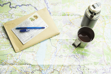 Map & Travel. thermos mug camp, an envelope and a postcard from your trip. on the map background