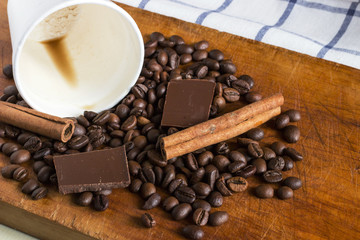 Coffee in white plastic glass with background of coffee beans, chocolate chunks and cinnamon sticks