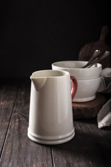 Ceramic white jug with red handle on dark wooden table. Pitcher.