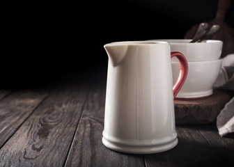 Ceramic white jug with red handle on dark wooden table. Pitcher.