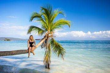 young lady sitting on palm tree over blue sea