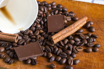 Coffee in white plastic glass with background of coffee beans, chocolate chunks and cinnamon sticks