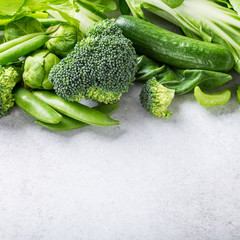 Background with assorted green vegetables, salad, broccoli, cucumber, peas and Brussels sprouts on light gray stone table top. Healthy food concept with copy space.