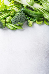 Background with assorted green vegetables, salad, broccoli, cucumber, peas and Brussels sprouts on light gray stone table top. Healthy food concept with copy space.