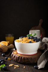 Healthy breakfast with corn flakes, berries and milk on old dark wooden background. Copy space.