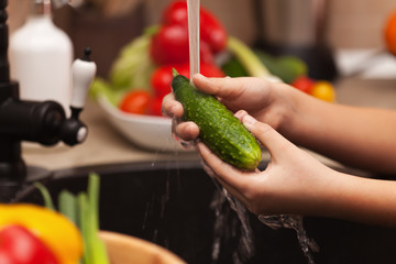Child hands washing a cucumber at the sink, shallow depth