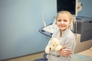 The girl with a soft toy in the hospital on a background of ultrasound machines, smiling and playing