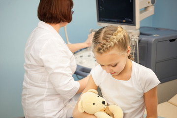 The girl with a soft toy in the hospital on a background of ultrasound machines, smiling and playing