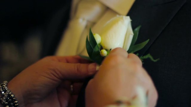 White rose boutonniere being pinned onto a grooms suit.