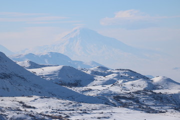 Fototapeta na wymiar Fantastic winter panorama of the range of mountains with the peak of Ararat at the background. It's a great success to see the peak of Ararat in winter as it is almost always covered with clouds