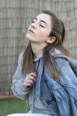 Young woman with a denim jacket over her shoulder and eyes closed.