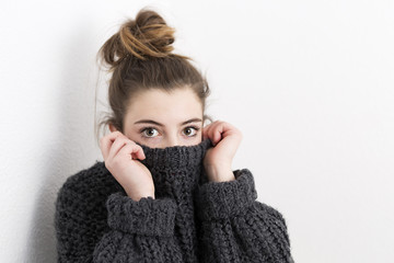 Young woman covering her mouth with a sweater on a white background.