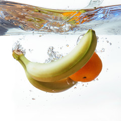 bananas and orange fell into the water, isolated on white.