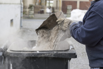 man throwing ashes in a trash bin.