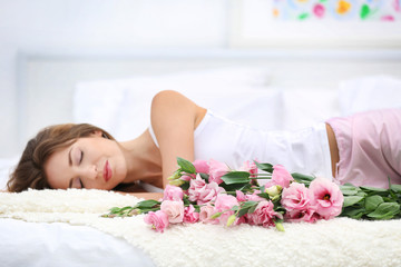 Obraz na płótnie Canvas Young cheerful woman with beautiful bouquet of eustoma flowers lying on bed at home