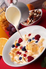 Pouring milk into tasty cornflakes on red background